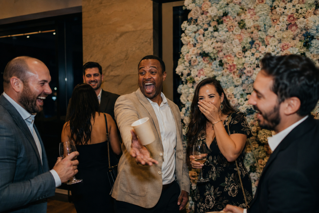 Guests laughing over an unplanned moment beside an unused flower-wall photo backdrop.