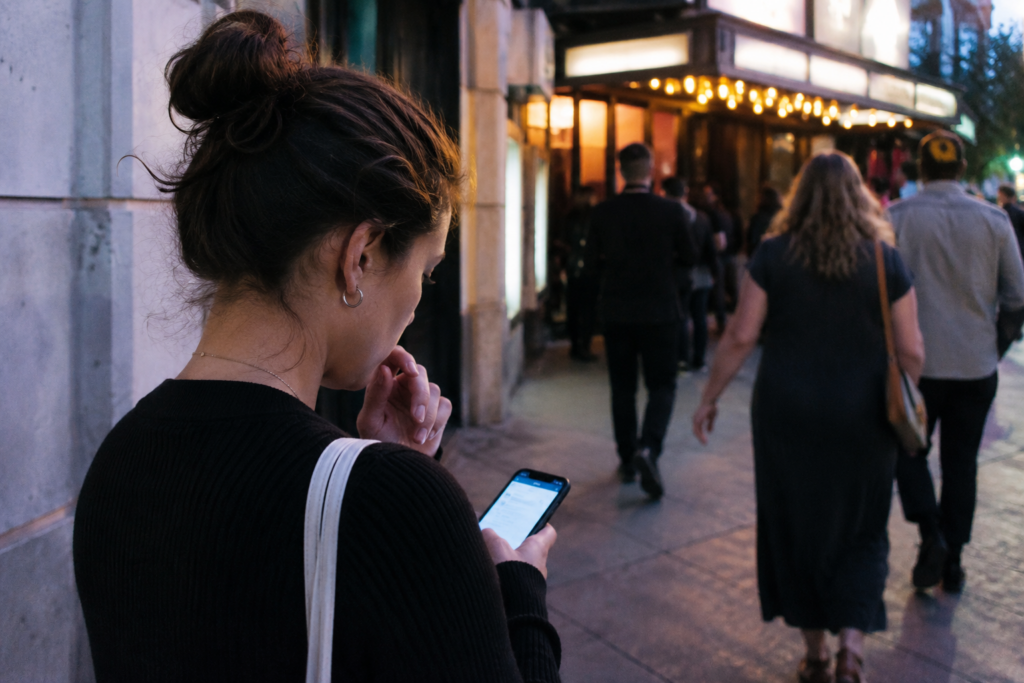 Woman checking a ticket page on her phone outside a Los Angeles venue at dusk.